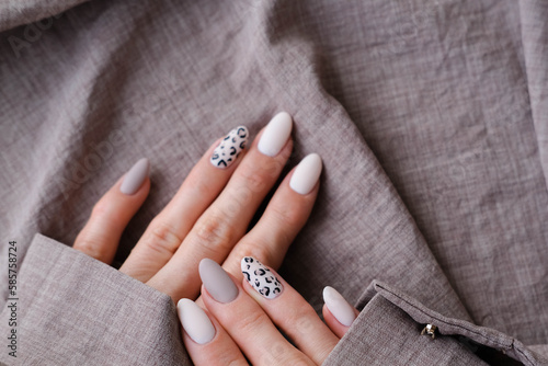 A woman s hand with a beautiful manicure holds a beige fabric. Autumn trend  beige color polishing with leopard pattern on nails with gel polish  shellac.