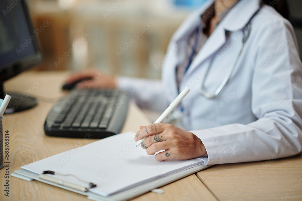 Fototapeta premium Cropped image of physician checking patients medical history in database on computer and taking notes