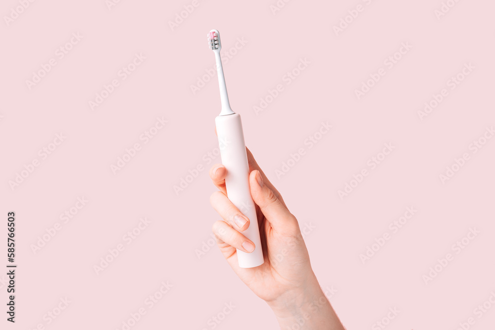Electric toothbrush of pink color in female hand against pink background. Electric toothbrush of pink color in female hand against pink background.