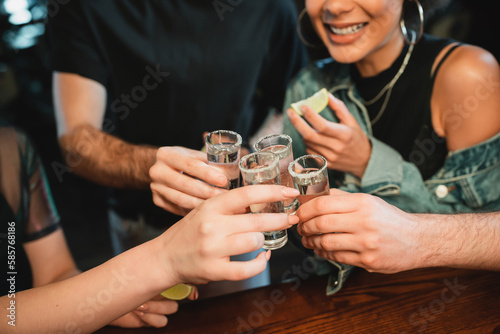 cropped view of multiethnic people holding tequila shots with salt on glasses in bar.