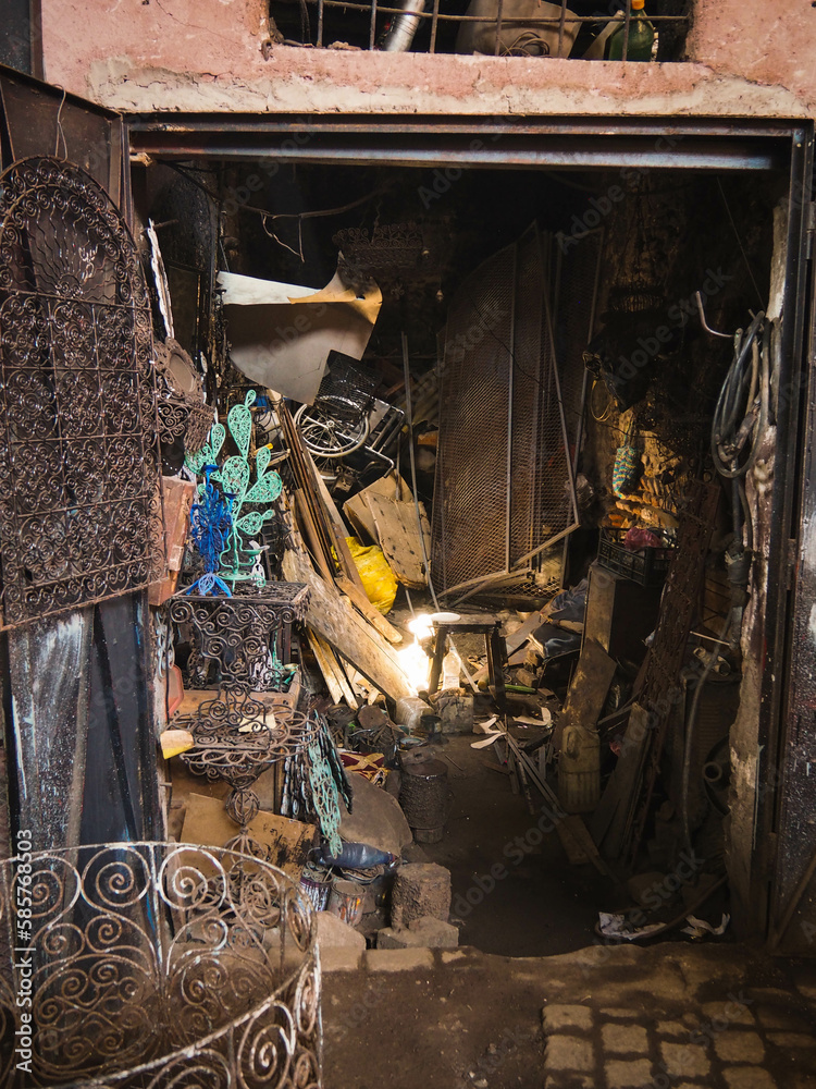 Rays of light in a dark, crowded garage in the busy Souk market alley selling and welding metal wares in the heart of the Medina of Marrakech, Morocco, dark street with sunlight
