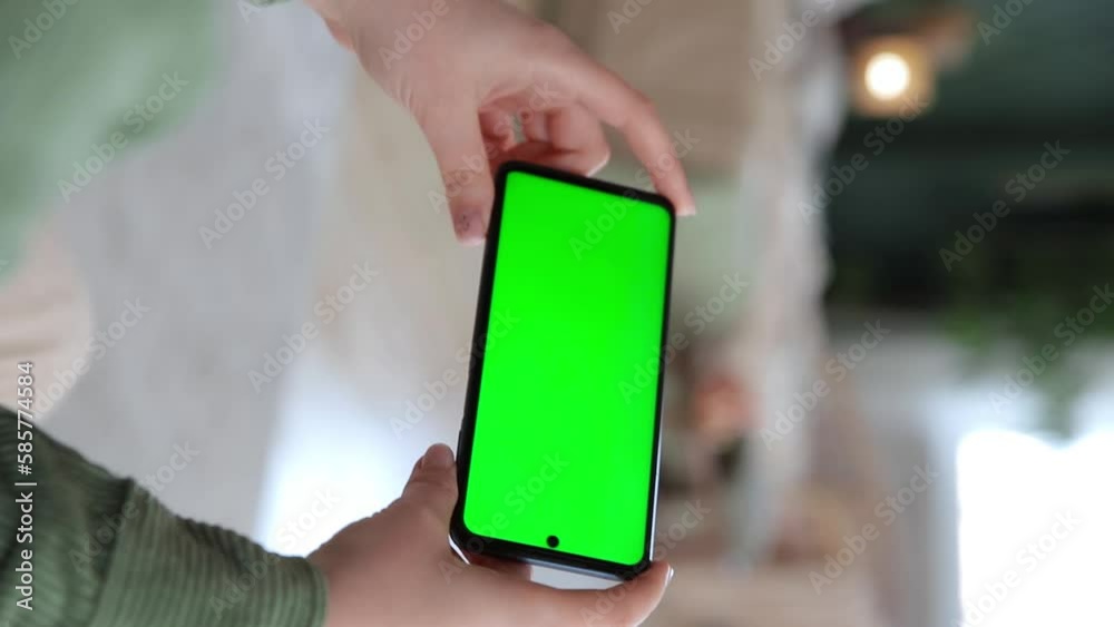 Vertical video. Handheld camera mock up. Close up view of woman hand using horizontal smartphone with key green screen. Chroma key mock up for applications of streaming services. Selective focus Vertical video. Handheld camera mock up. Close up view of woman hand using horizontal smartphone with key green screen. Chroma key mock up for applications of streaming services. Selective focus