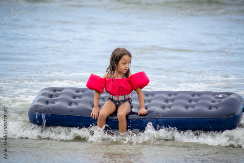 Criança brincando na praia com boia flutuante nas ondas do mar na cor azul e rosa. photo