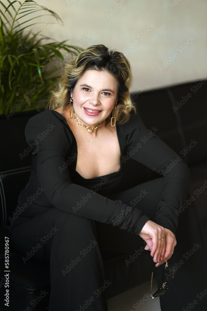 Fototapeta premium A smiling woman in a black suit sits holding glasses.