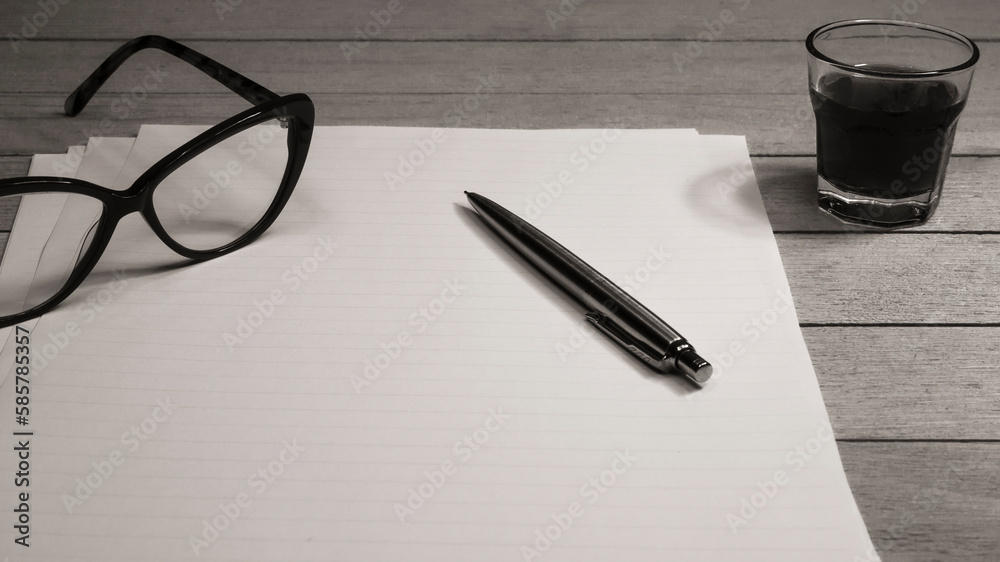 Fototapeta premium Paper sheets on the desk. Desaturated image of a wooden desk with papers, pen, eyeglass and glass.