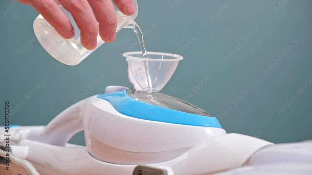 A man pours distilled water into a steam cleaner through a funnel