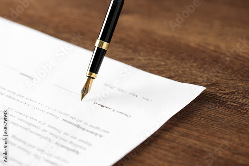 Writing on document with fountain pen at wooden table, closeup. Notary contract