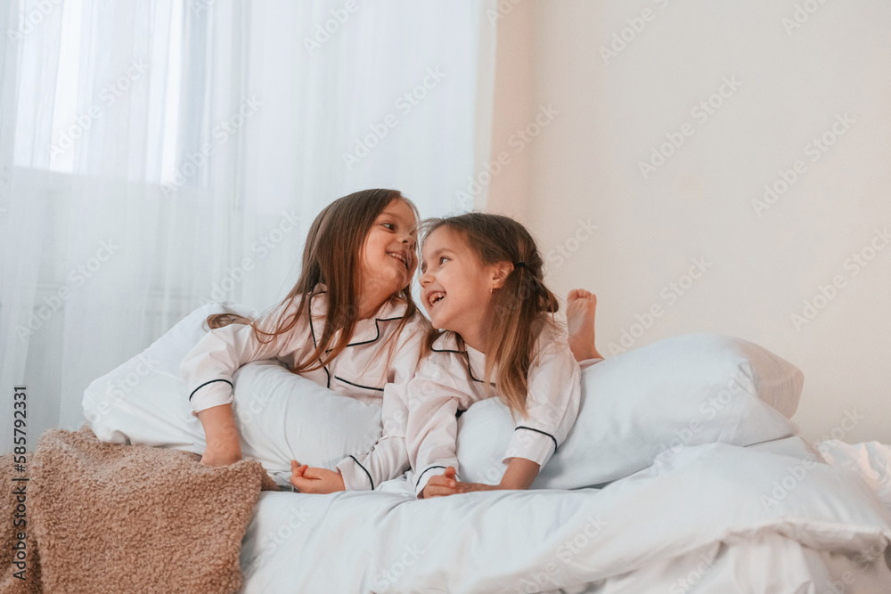 Lying down on the bed. Two little girls are playing and having fun together in domestic room Lying down on the bed. Two little girls are playing and having fun together in domestic room