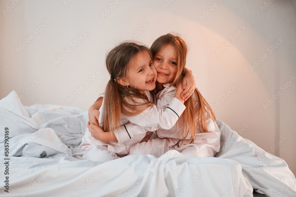 Embracing each other on the bed. Two little girls are playing and having fun together in domestic room Embracing each other on the bed. Two little girls are playing and having fun together in domestic room