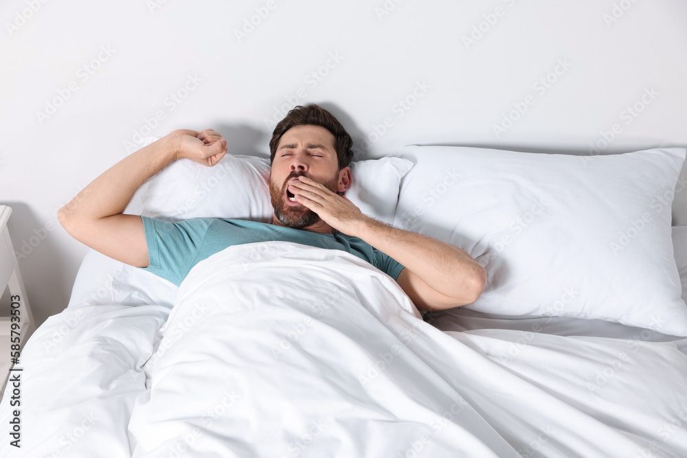 Handsome man yawning while lying on pillow in bed at home Handsome man yawning while lying on pillow in bed at home