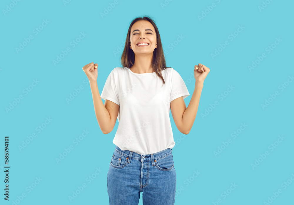 Yes, yes, yes. Studio shot of happy pretty young woman in white Tshirt and blue jeans standing isolated on blue background, celebrating success, clenching fists, doing yes gesture and smiling Yes, yes, yes. Studio shot of happy pretty young woman in white Tshirt and blue jeans standing isolated on blue background, celebrating success, clenching fists, doing yes gesture and smiling