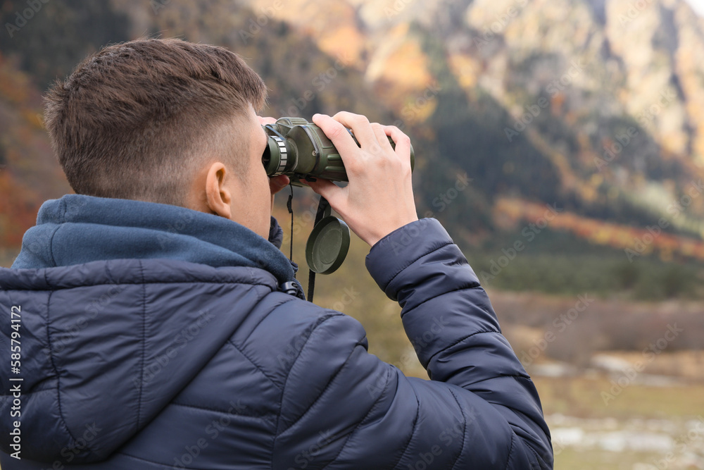 Boy looking through binoculars in beautiful mountains, back view