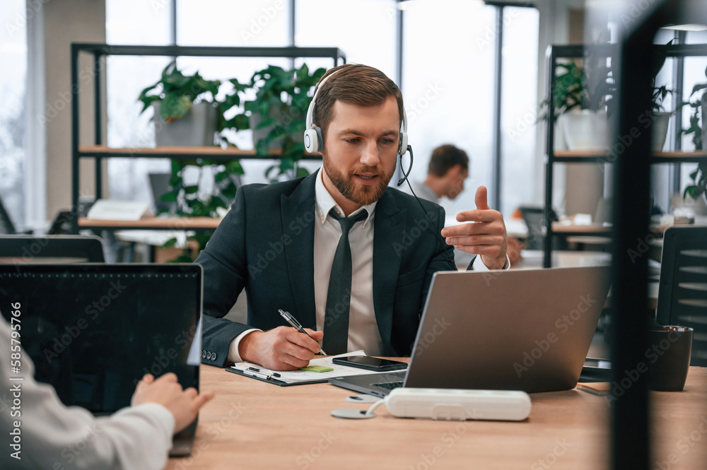 Man in suit is working in the office by laptop. With woman that siting by the table Man in suit is working in the office by laptop. With woman that siting by the table