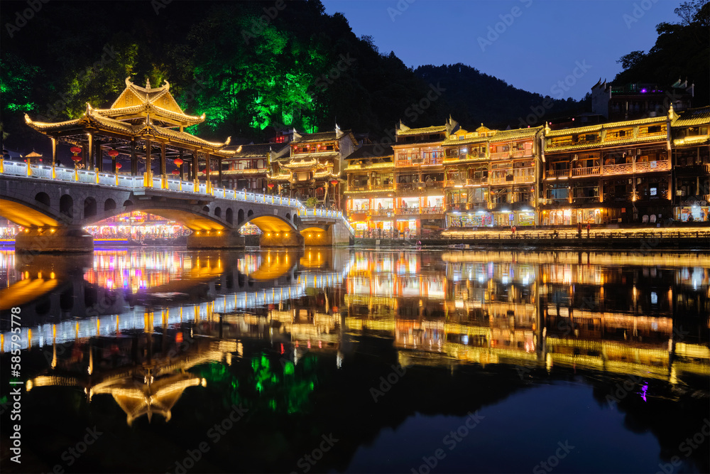 Fototapeta premium Chinese tourist attraction destination - Feng Huang Ancient Town (Phoenix Ancient Town) on Tuo Jiang River with bridge illuminated at night. Hunan Province, China