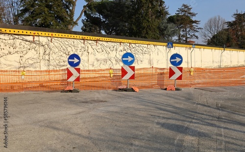 Several directional road signs and warning lights in front of plastic barrier before a temporary closed road. Background for copy space.