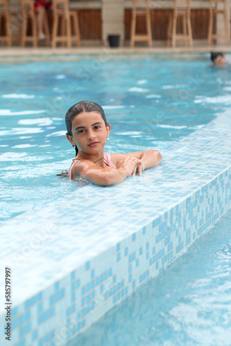 A beautiful young girl in the swimming pool. Adorable little girl is enjoying her time on a sunny day.  Traveling and vacation concept