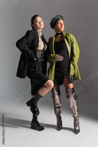 Full length of fashionable multiethnic models in jacket and coat posing on grey background.