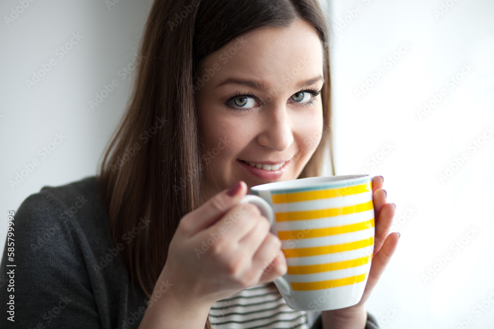 Beautiful young woman drinking tea by the window