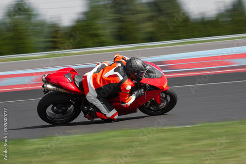 A motorcycle rider in leather suit riding on a red sport motorcycle through a corner at high speed. Leaning from the bike and dragging a knee. 