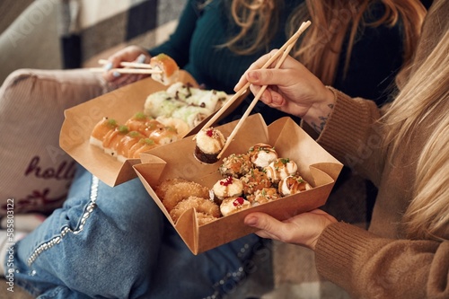 Two women are sitting and eating sushi indoors together