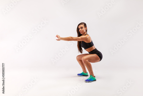 Workout. A young woman performs a deep squat exercise against a gray background in the studio. Space for copying