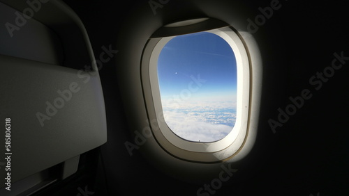 Airplane window in the air high above. Passenger plane POV looking out at beautiful blue sky view