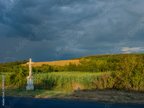 Crucifix in landscape with sunlight but also storm clouds