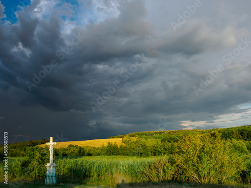 Crucifix in landscape with sunlight but also storm clouds