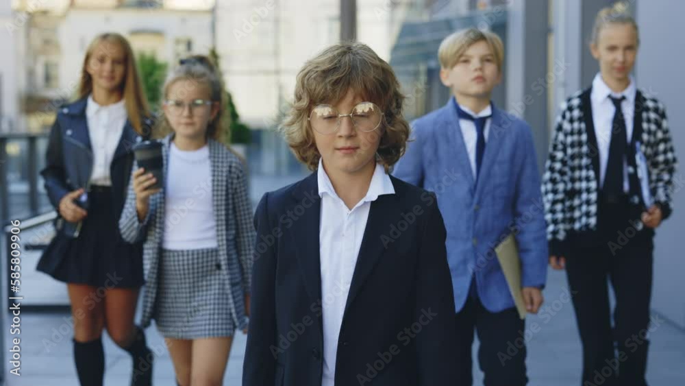 Group of the young little business people walking outdoors near office building looking at camera. Successful business team. Kids as a adults. Entrepreneurs concept Group of the young little business people walking outdoors near office building looking at camera. Successful business team. Kids as a adults. Entrepreneurs concept