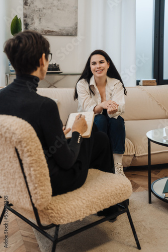 Canvas Print Psychologist writing down notes during therapy session with smiling woman