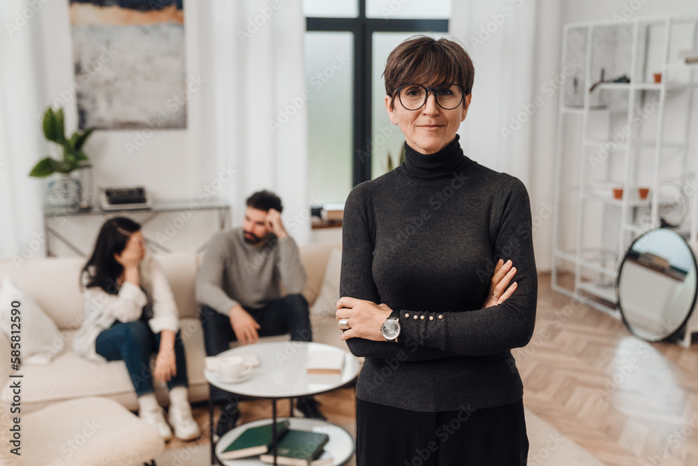 © Drobot Dean - Female psychologist standing in her office with married couple on the background