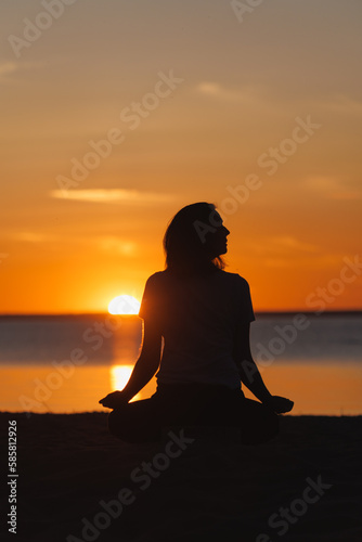 yoga meditation  silhouette of woman at sunset in lotus position. health recreation and sports  outdoor training. poster  postcard. person is engaged in breathing practices on seashore. mental health