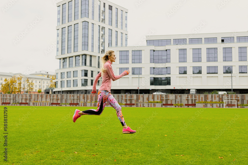 Running training at the stadium. A young woman in a bright tracksuit practicing running technique
