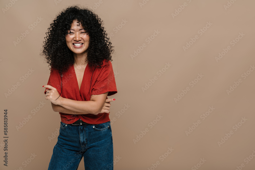 Beautiful asian woman smiling at camera while standing with arms folded isolated over beige background Beautiful asian woman smiling at camera while standing with arms folded isolated over beige background