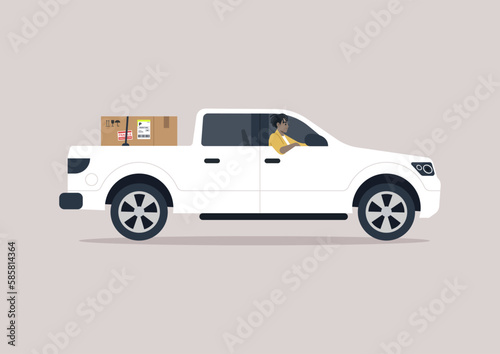 A young driver of a pickup truck driving with one elbow hanging out of the window, a cardboard box in the trunk