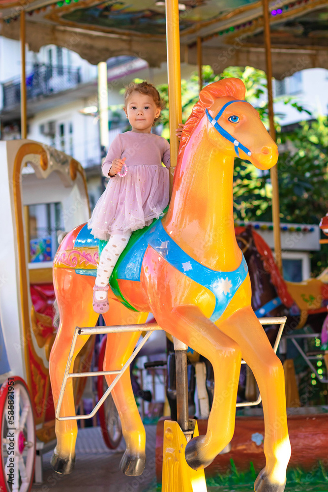 kid riding on a merry go round. Little girl playing on carousel, summer fun, happy childhood and vacation concept