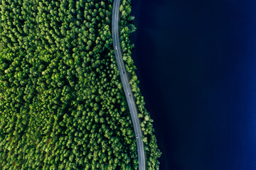Aerial view of road in green woods and blue lakes water in Finland