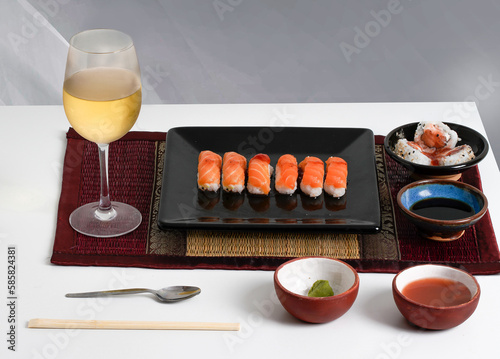 Sushi sobre plato negro con salsa agridulce, soja, copa de vino blanco, salmón rosado. 