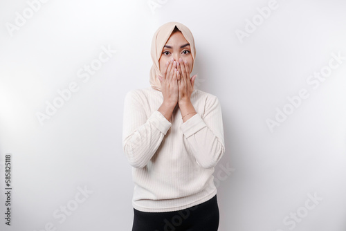 Portrait of a young Asian Muslim woman wearing a headscarf is tell be quiet, shushing with serious face, hush with finger pressed to lips, isolated by white background photo
