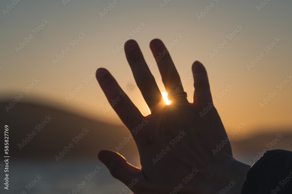 The sun shining between the fingers of a woman's palm at sunset on the seashore