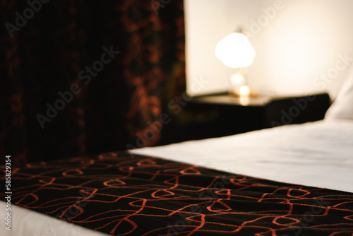 Night table with lamp besides bed out of focus