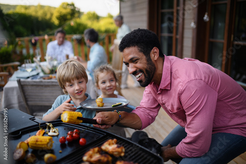 Multi generation family having bbq party outside in the backyard on patio.