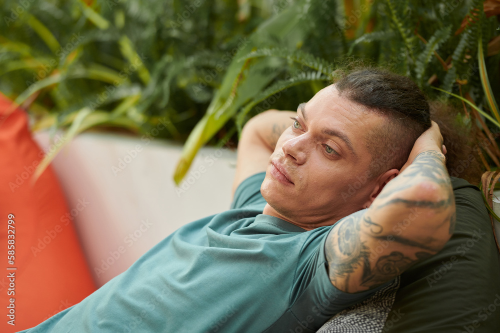 Pensive young man leaning back in armchair when resting in outdoor cafe Pensive young man leaning back in armchair when resting in outdoor cafe