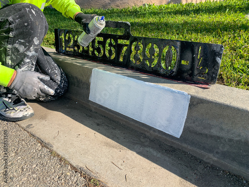 City worker painting address on street curbs using stencil numbers with white and blank paint
