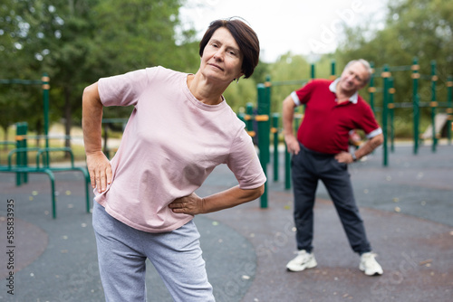 Aged man and woman practicing gymnastics in open-air sports area