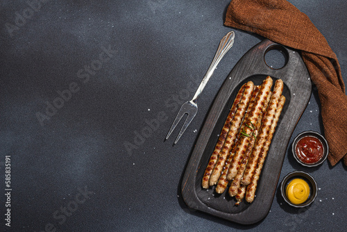 Roasted pork meat sausages on wooden board. Set of sauces, traditional food for picnic or BBQ