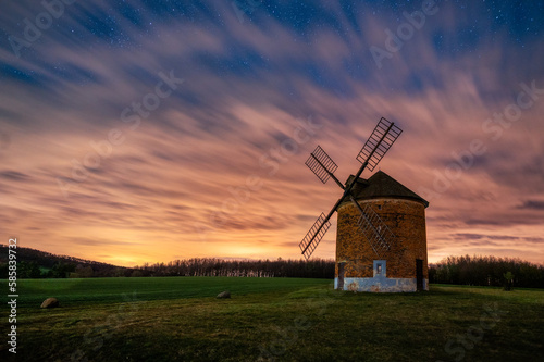 A beautiful Dutch-type windmill in the village of Chvalkovice in South Moravia. Night photograph of windmill with starry sky and reddish light. 