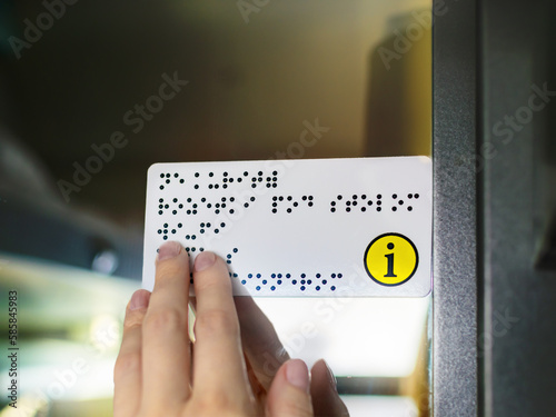 Hand of a person with blindness touches and reads Braille text plate with his hands on the door of a public transport. Close-up of a womans fingers touching the relief of points.