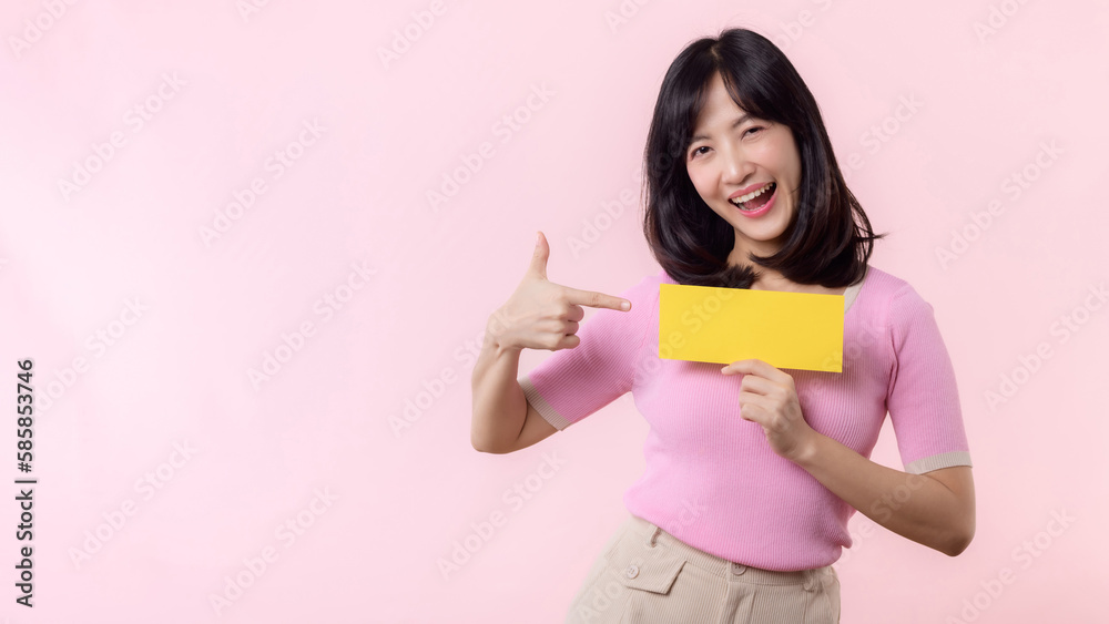Portrait happy young woman model holding and showing blank space paper for advertisement information message poster with thumb up or point finger gesture isolated on pink pastel studio background. Portrait happy young woman model holding and showing blank space paper for advertisement information message poster with thumb up or point finger gesture isolated on pink pastel studio background.
