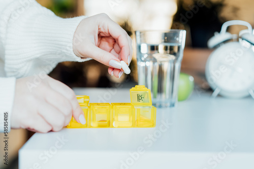 Woman's hands sorting pills into pills organizer. Close up medical pill box with daily doses of medicines. Time for Antioxidant diet vitamin supplements for health and beauty care, biohacking concept.